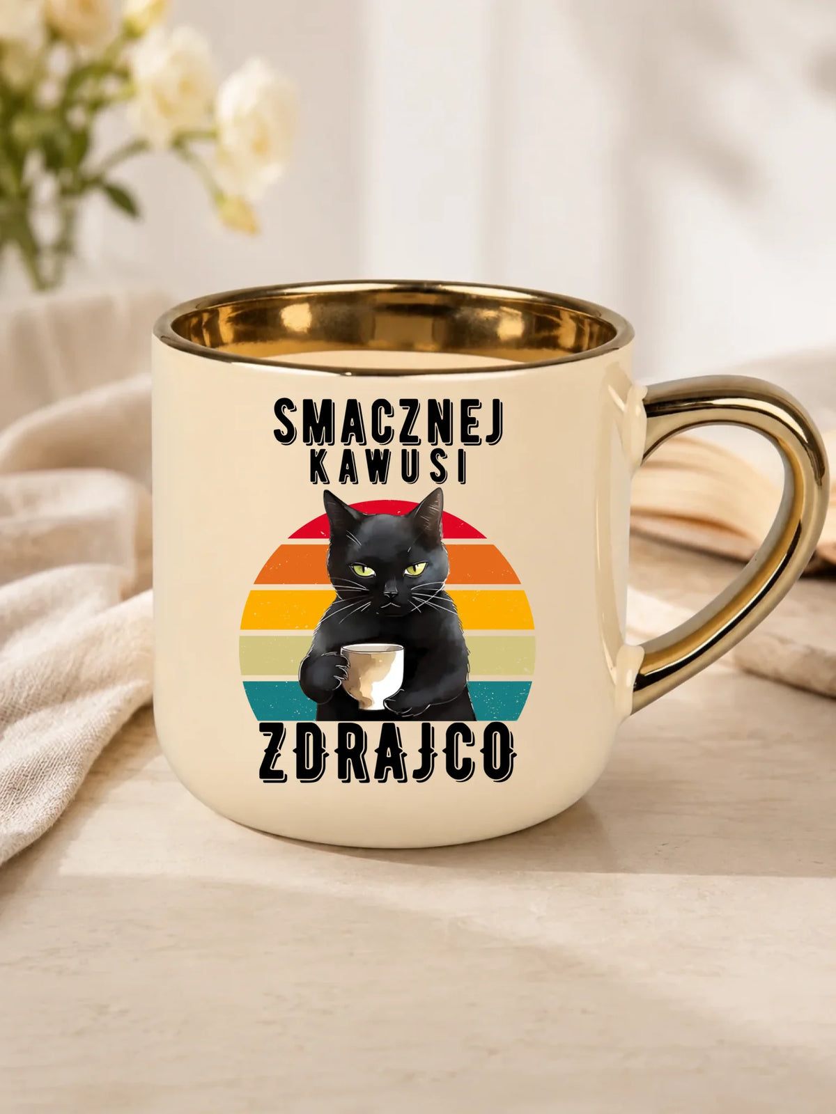 Prezent na odejście z pracy dla kolegi, kremowy kubek ze złotym rantem na stole, wzór Smacznej kawusi zdrajco, czarny kot.