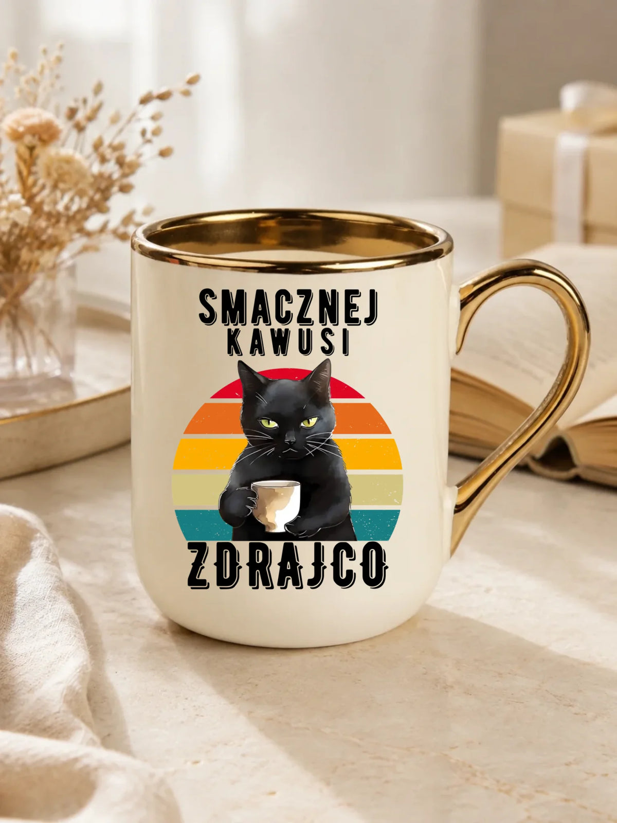 Upominek na odejście z pracy dla kolegi, kubek ze złotym rantem na stole, wzór Smacznej kawusi zdrajco, czarny kot.
